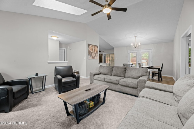 carpeted living room with ceiling fan with notable chandelier, vaulted ceiling with skylight, and french doors