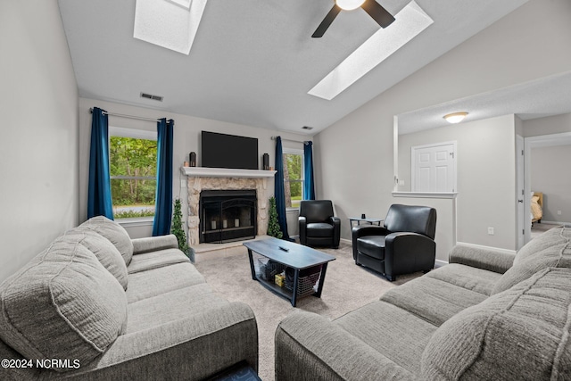 carpeted living room with ceiling fan, a skylight, a fireplace, and high vaulted ceiling