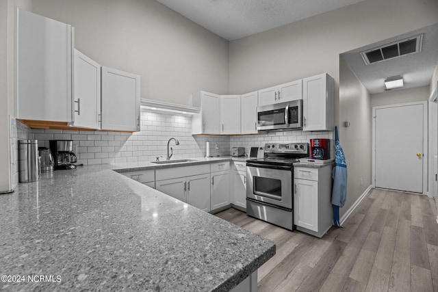 kitchen with white cabinets, stainless steel appliances, a textured ceiling, light hardwood / wood-style flooring, and sink