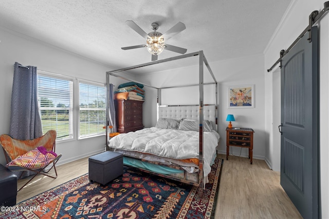 bedroom featuring a barn door, ceiling fan, a textured ceiling, and light wood-type flooring