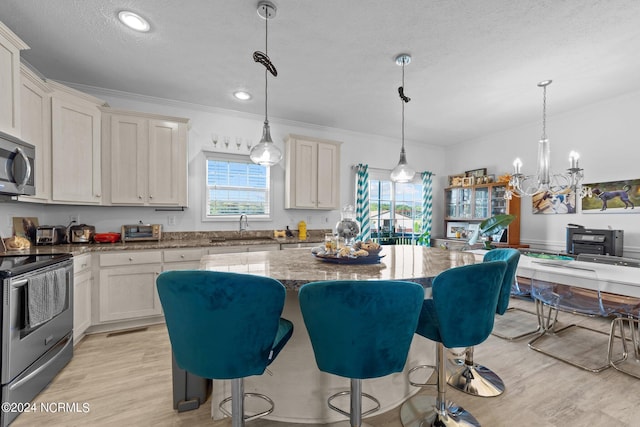 kitchen featuring sink, light hardwood / wood-style floors, appliances with stainless steel finishes, decorative light fixtures, and a kitchen island