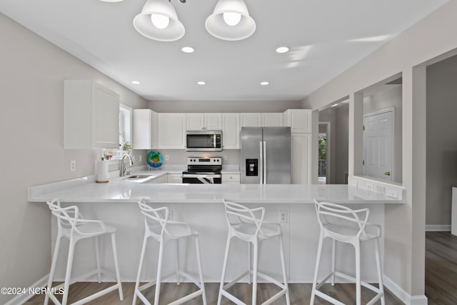 kitchen featuring kitchen peninsula, appliances with stainless steel finishes, a kitchen breakfast bar, sink, and white cabinets