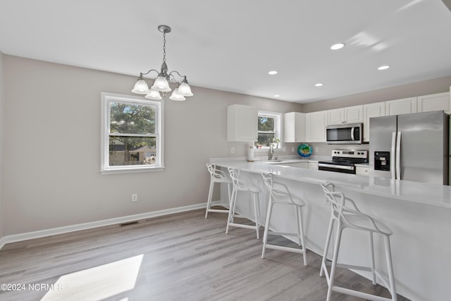 kitchen featuring a kitchen bar, kitchen peninsula, stainless steel appliances, light hardwood / wood-style floors, and white cabinetry