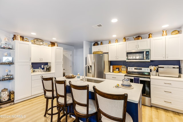 kitchen with an island with sink, light wood-type flooring, a breakfast bar, and appliances with stainless steel finishes