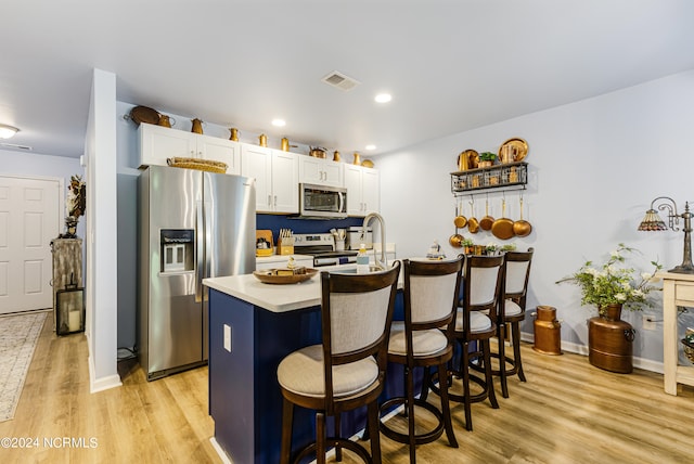 kitchen featuring a center island with sink, light hardwood / wood-style flooring, white cabinetry, stainless steel appliances, and a breakfast bar area