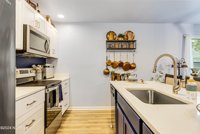 kitchen with light stone counters, sink, white cabinetry, stainless steel appliances, and light hardwood / wood-style floors