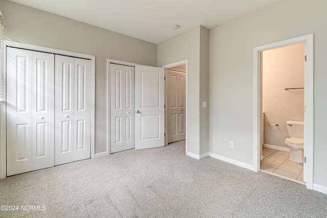 unfurnished bedroom featuring light carpet, two closets, and ensuite bath