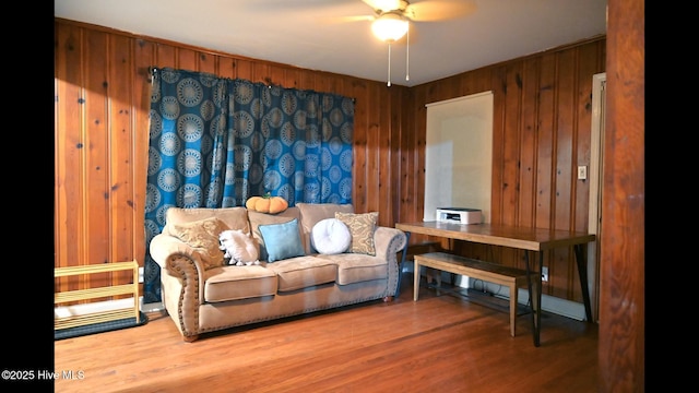 living room featuring ceiling fan, hardwood / wood-style floors, and wooden walls