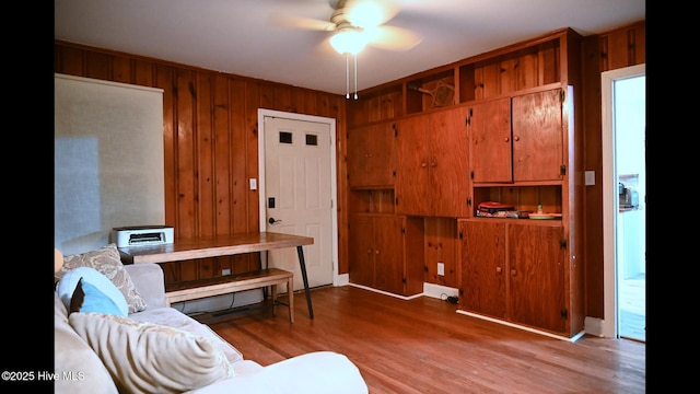 living room with ceiling fan, light hardwood / wood-style flooring, and wood walls