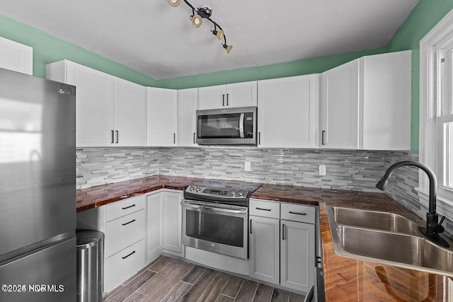 kitchen with sink, appliances with stainless steel finishes, white cabinetry, wood counters, and decorative backsplash