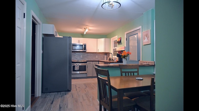 kitchen featuring sink, white cabinetry, backsplash, stainless steel appliances, and light wood-type flooring