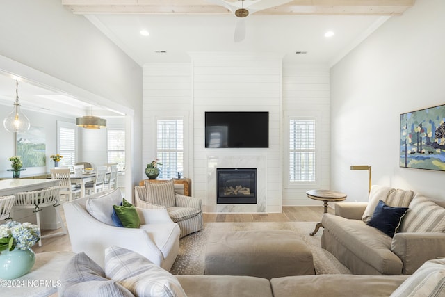 living room featuring ceiling fan, a large fireplace, light hardwood / wood-style floors, ornamental molding, and beam ceiling