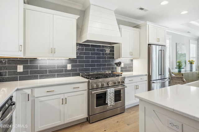 kitchen featuring high quality appliances, ornamental molding, custom range hood, and white cabinetry