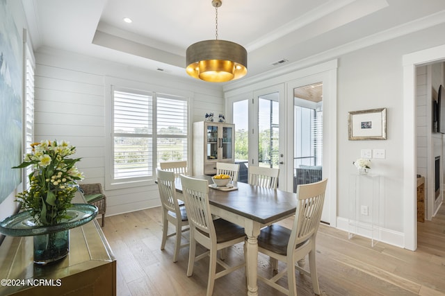 dining area with ornamental molding, light wood-type flooring, french doors, and a raised ceiling