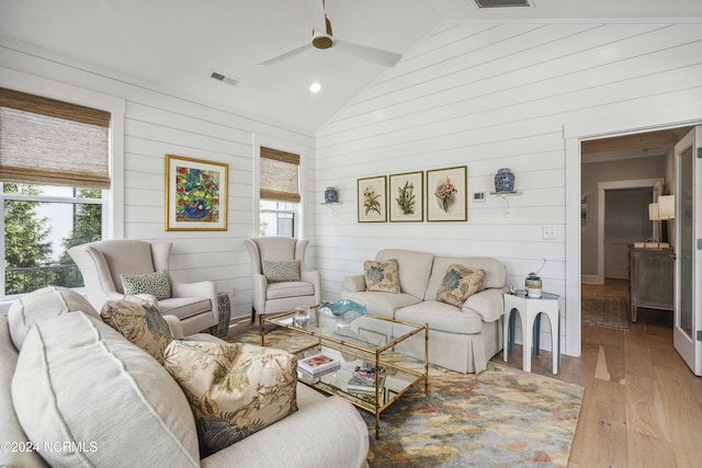 living room featuring vaulted ceiling, light hardwood / wood-style flooring, a wealth of natural light, and wooden walls