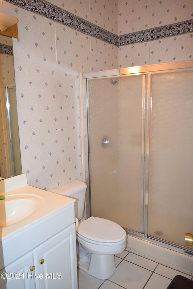 bathroom with tile patterned floors, a shower with door, vanity, and toilet