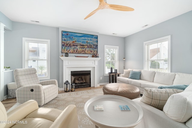 living room featuring a tiled fireplace, ceiling fan, and plenty of natural light