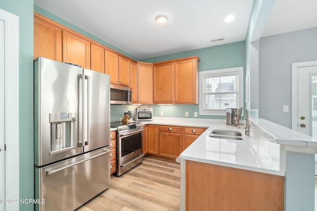 kitchen featuring light stone counters, light hardwood / wood-style floors, sink, kitchen peninsula, and stainless steel appliances