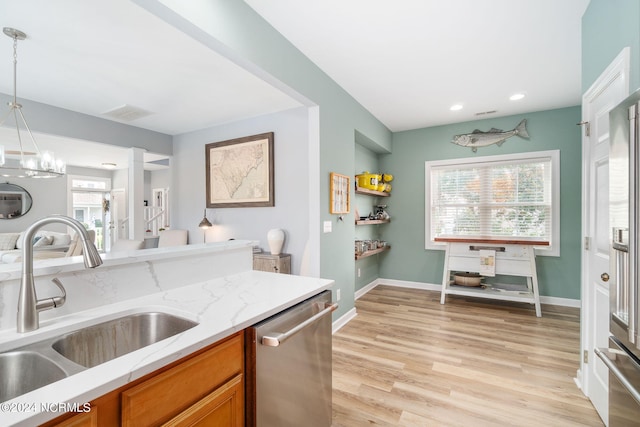 kitchen with light hardwood / wood-style floors, light stone countertops, pendant lighting, stainless steel dishwasher, and sink