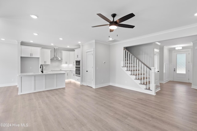 kitchen featuring light hardwood / wood-style floors, white cabinetry, wall chimney exhaust hood, and an island with sink