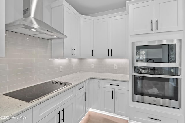 kitchen featuring decorative backsplash, light stone countertops, wall chimney exhaust hood, stainless steel appliances, and white cabinetry