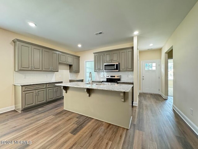 kitchen with appliances with stainless steel finishes, gray cabinetry, dark hardwood / wood-style flooring, and light stone counters