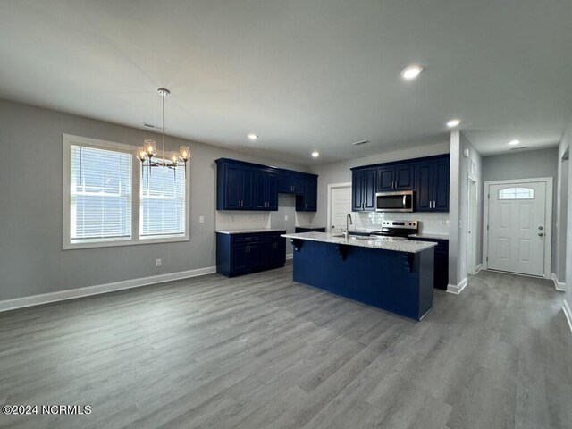 kitchen with an inviting chandelier, light wood-type flooring, an island with sink, and appliances with stainless steel finishes