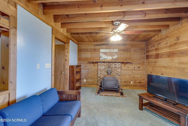 carpeted living room featuring beam ceiling, wood walls, a wood stove, and ceiling fan