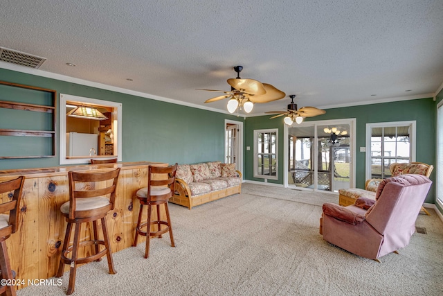 living room with ceiling fan, a textured ceiling, indoor bar, crown molding, and light colored carpet