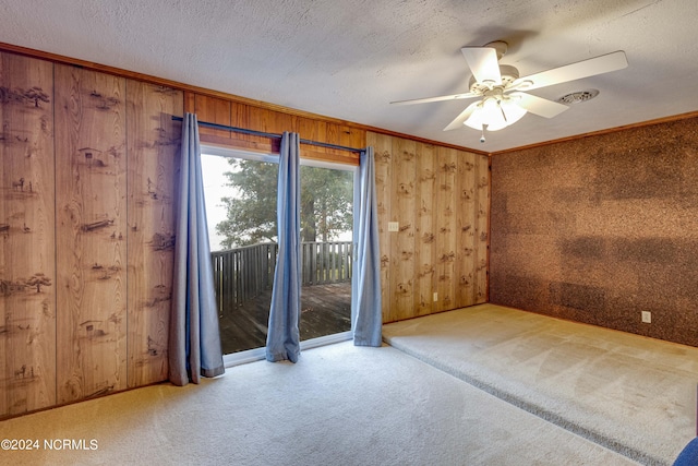 carpeted empty room with crown molding, wood walls, a textured ceiling, and ceiling fan