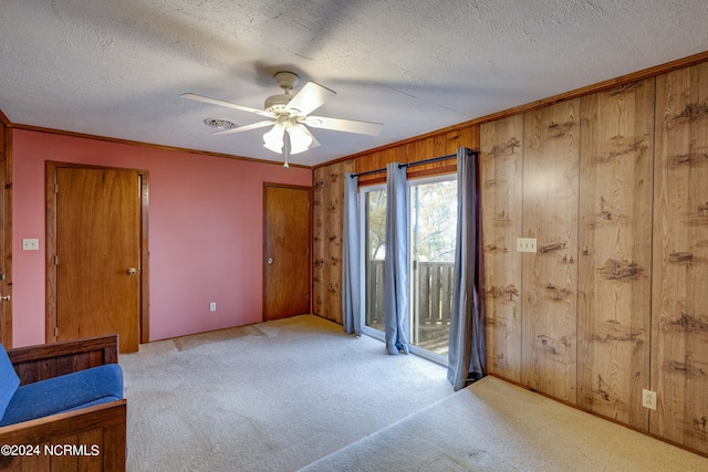 empty room featuring a textured ceiling, ceiling fan, light colored carpet, and wood walls