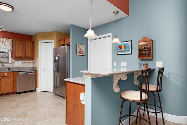 kitchen with brown cabinetry, a breakfast bar, a peninsula, stainless steel appliances, and decorative light fixtures