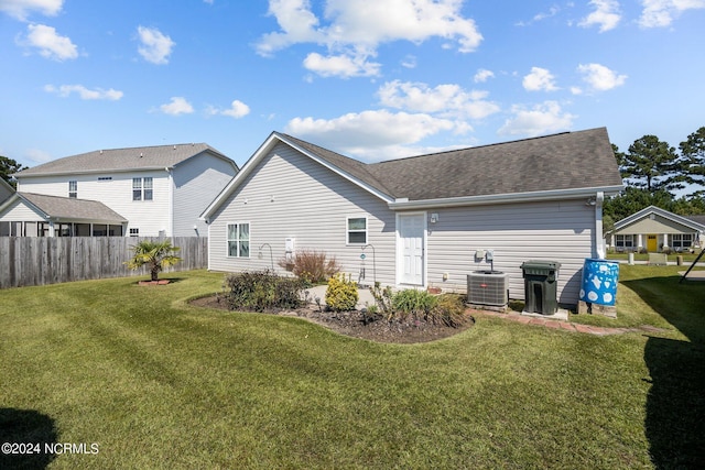 rear view of house with a lawn, central AC unit, and fence