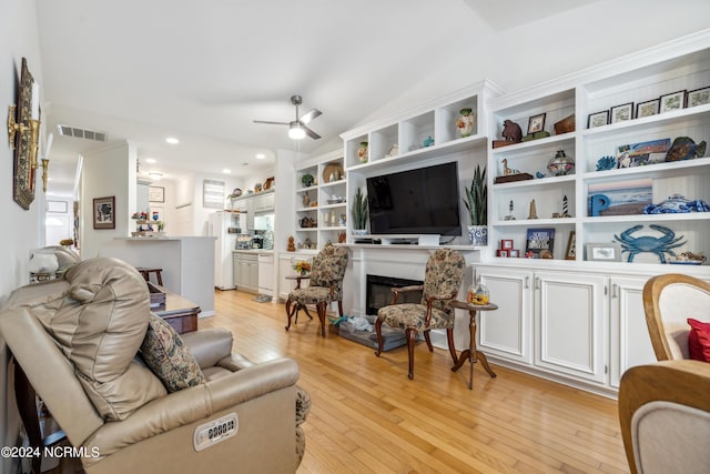 living room featuring vaulted ceiling, built in shelves, ceiling fan, and light hardwood / wood-style flooring