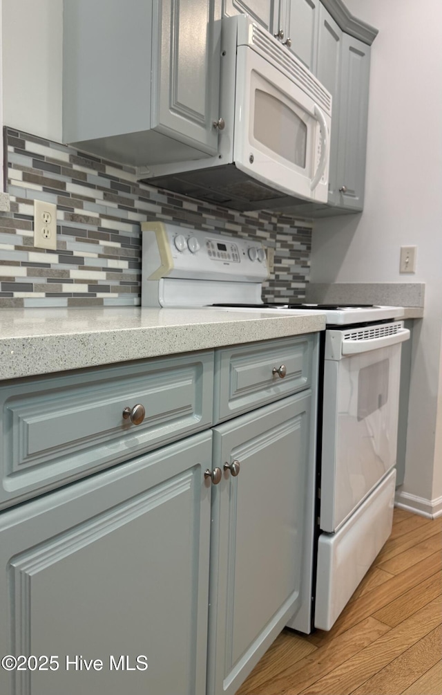 kitchen featuring tasteful backsplash, light wood-type flooring, gray cabinetry, and white appliances