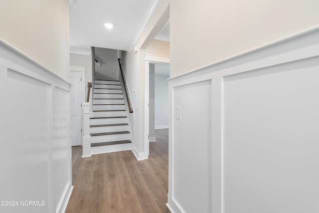 stairway with crown molding and wood-type flooring