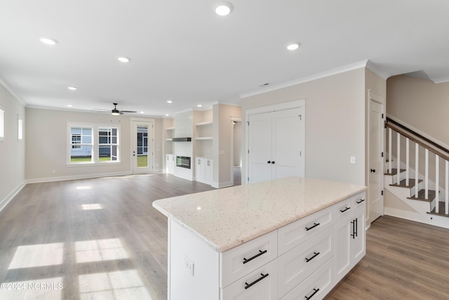 kitchen featuring a kitchen island, white cabinetry, hardwood / wood-style flooring, crown molding, and light stone counters