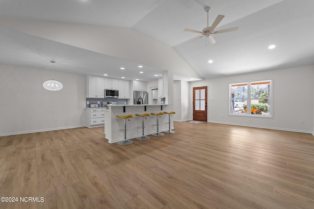 kitchen with lofted ceiling, a kitchen bar, white cabinetry, appliances with stainless steel finishes, and light hardwood / wood-style floors