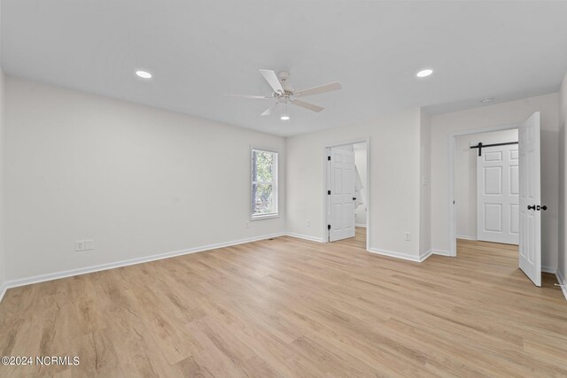 unfurnished bedroom with ensuite bath, a barn door, light hardwood / wood-style floors, and ceiling fan