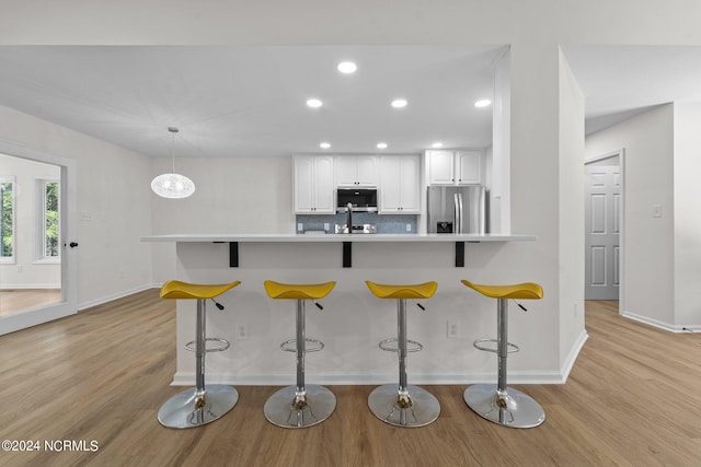 kitchen featuring kitchen peninsula, a breakfast bar, white cabinetry, light hardwood / wood-style floors, and stainless steel appliances