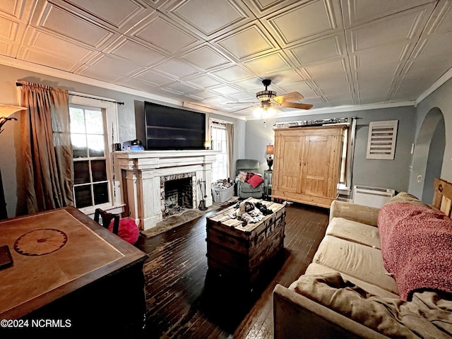 living room with ceiling fan, a brick fireplace, dark hardwood / wood-style flooring, and crown molding