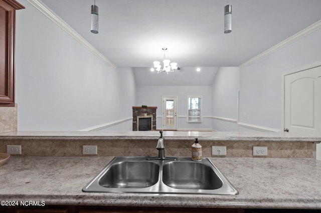 kitchen with lofted ceiling, sink, an inviting chandelier, a fireplace, and crown molding