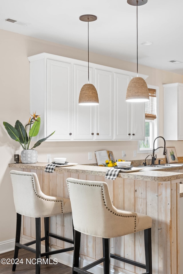 kitchen with sink, hanging light fixtures, a kitchen bar, white cabinets, and hardwood / wood-style flooring