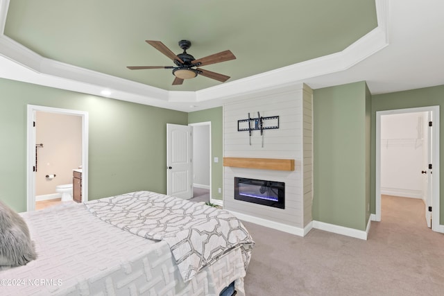 carpeted bedroom with a walk in closet, ceiling fan, a tray ceiling, a large fireplace, and a closet