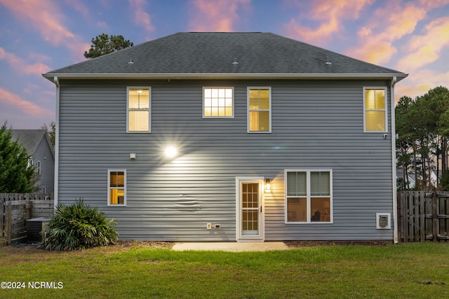 back house at dusk featuring a yard, a patio, and central air condition unit