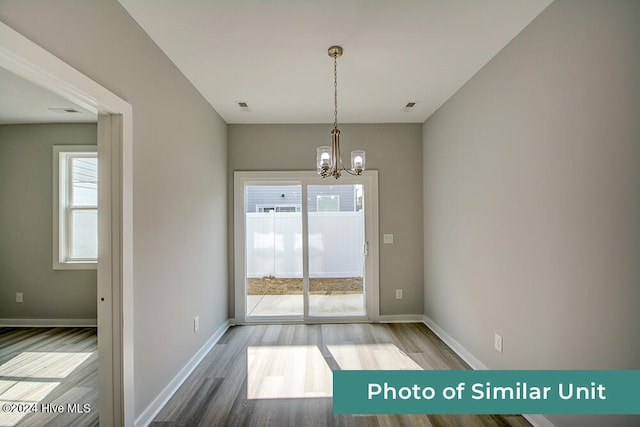 unfurnished dining area with wood finished floors, a chandelier, visible vents, and baseboards