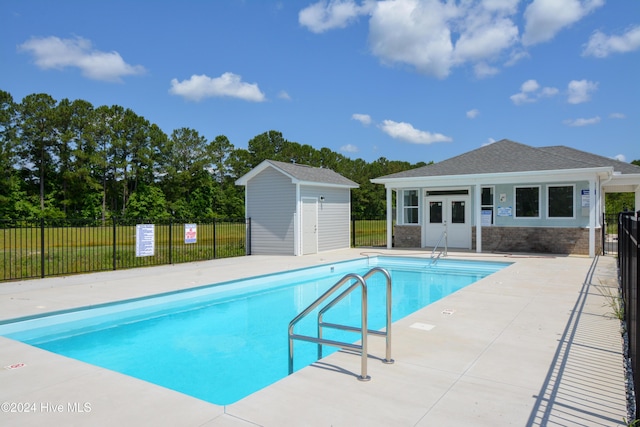 community pool with fence, an outbuilding, and a patio area