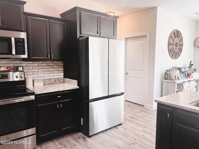 kitchen featuring decorative backsplash, appliances with stainless steel finishes, light hardwood / wood-style floors, and light stone countertops