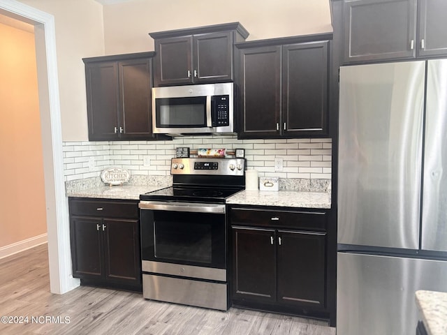 kitchen with light stone counters, decorative backsplash, light hardwood / wood-style flooring, and appliances with stainless steel finishes