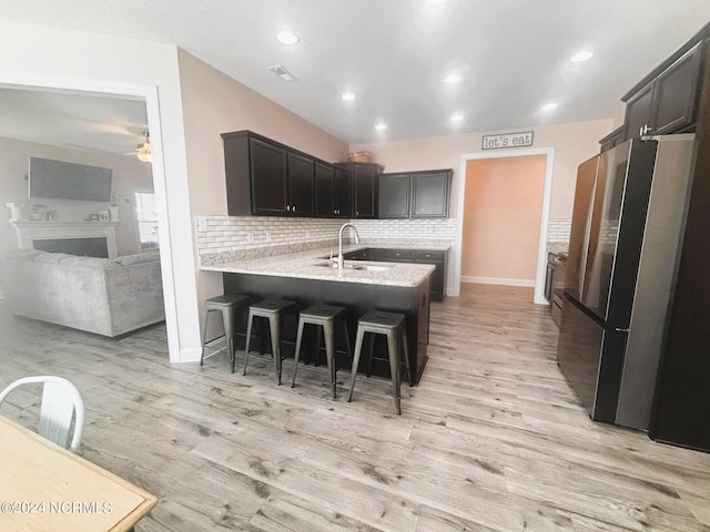 kitchen featuring a kitchen bar, kitchen peninsula, sink, light wood-type flooring, and stainless steel fridge